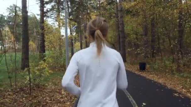 Unga blonda kvinnan kör i höst park. — Stockvideo