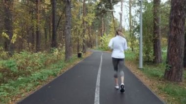 Sonbahar parkta çalışan sarışın genç kadın üzerinde arkadan görünüm.