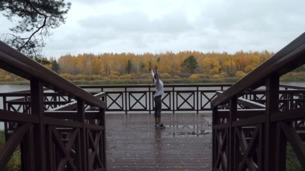 Sportliche Frau wärmt sich vor dem Joggen auf dem Holzsteg auf. — Stockvideo