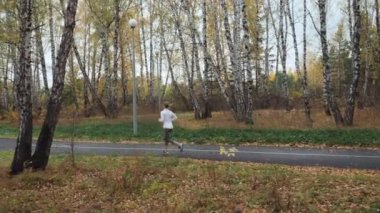 Rusya, Tyumen - 08 Ekim 2018. Gilyevskaya roscha. Sonbahar parkta çalışan sarışın genç kadın genel planı. Spor kavram. Ağır çekim 60 Fps. Steadicam atış stabilize.