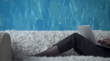 Odasında kanepede otururken dizüstü bilgisayar üzerinde çalışan kadın.