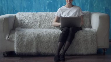 Odasında kanepede otururken dizüstü bilgisayar üzerinde çalışan kadın.