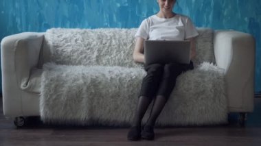Odasında kanepede otururken dizüstü bilgisayar üzerinde çalışan kadın.