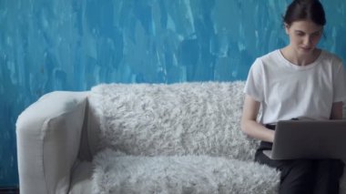 Odasında kanepede otururken dizüstü bilgisayar üzerinde çalışan kadın.
