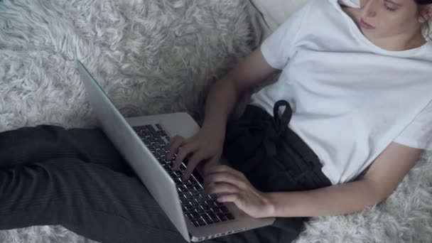 Женщина, работающая на ноутбуке, лежа дома на диване . — стоковое видео