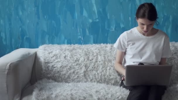 룸에 소파에 앉아있는 동안 노트북 컴퓨터에서 작업 하는 여자. — 비디오