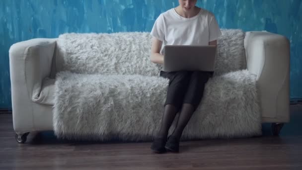Mujer trabajando en el ordenador portátil mientras está sentado en el sofá en la habitación . — Vídeos de Stock