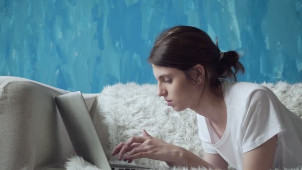 Woman using laptop at home while lying on the couch. — Stock Video