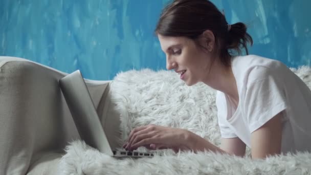 Uśmiechnięta kobieta za pomocą laptopa w domu, leżąc na kanapie. — Wideo stockowe