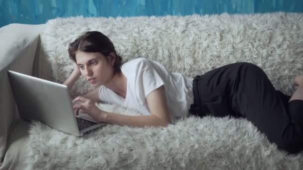 Leende kvinna använder laptop hemma liggandes på soffan. — Stockvideo