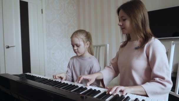Joven maestra con una niña linda tocando en el piano eléctrico . — Vídeos de Stock