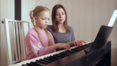 Genç bir kadın küçük bir kıza piyano çalmayı öğretiyor..