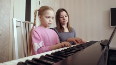 Genç bir kadın küçük bir kıza piyano çalmayı öğretiyor..