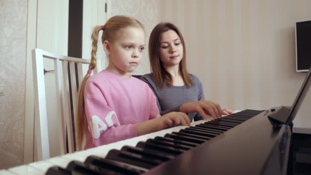 Młoda kobieta uczy dziewczynkę grać na pianinie.. — Wideo stockowe