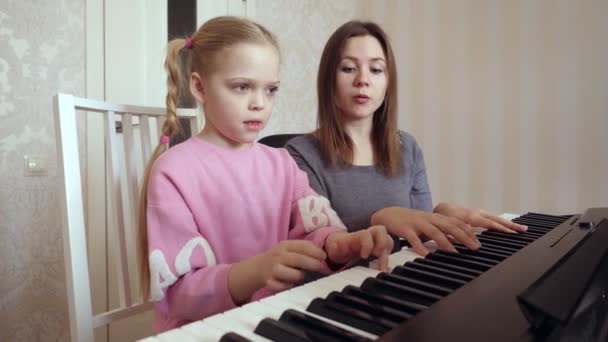 Mujer joven enseña a niña a tocar el piano . — Vídeos de Stock