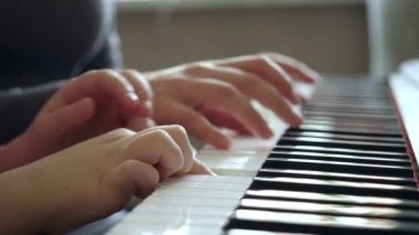 Genç bir kadın küçük bir kıza piyano çalmayı öğretiyor..