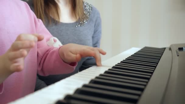 Mladá žena učí holčičku hrát na klavír. — Stock video