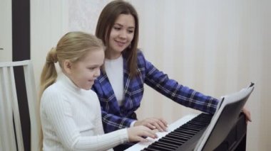 Genç öğretmen ve küçük tatlı kız elektrikli piyanoda oynuyorlar..