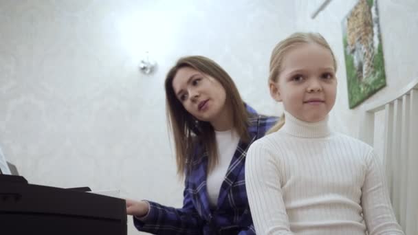 Joven profesora con la niña linda comprueba el oído para la música . — Vídeo de stock