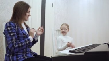 Genç öğretmen ve küçük tatlı kız elektrikli piyanoda oynuyorlar..