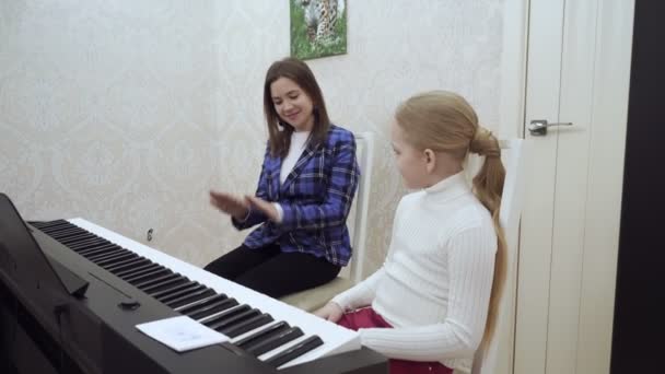 전기 ' 피아노 " 위에서 놀고 있는 귀여운 소녀와 함께 있는 어린 교사. — 비디오