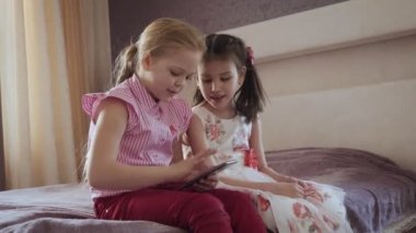 Yatak odasında yatakta oturan akıllı telefon kullanan iki küçük kız.
