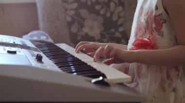 Tanınmayan küçük kız elektrikli piyano çalmak için okuyor.