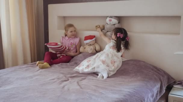 Twee kleine meisjes samen spelen op het bed met knuffels. — Stockvideo