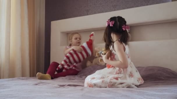 Två små flickor leker tillsammans på sängen med fyllda leksaker. — Stockvideo
