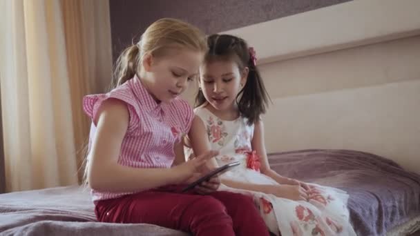 Yatak odasında yatakta oturan akıllı telefon kullanan iki küçük kız. — Stok video