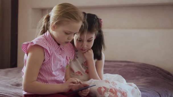 Dos niñas utilizando el teléfono inteligente sentado en la cama en el dormitorio . — Vídeo de stock