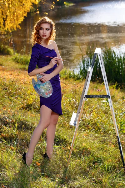 Young woman in sexy dress painting outdoors in autumn park. — Stock Photo, Image