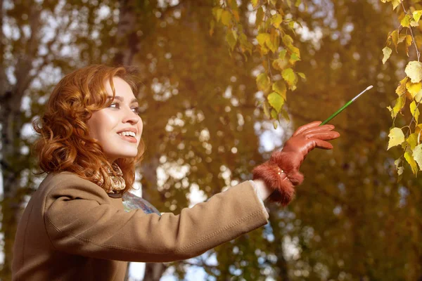 Belle femme avec palette et pinceau peint les feuilles de couleurs sur les arbres — Photo