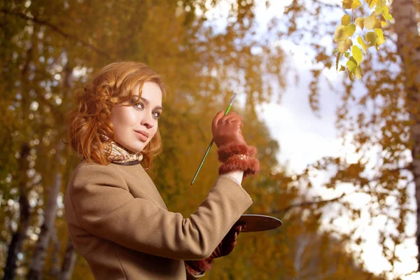 Belle femme avec palette et pinceau peint les feuilles de couleurs sur les arbres — Photo