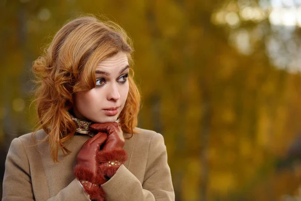 Stylish woman in beige coat and gloves standing in autumn yellow park. — Stock Photo, Image