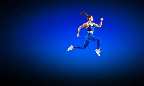 Junge Läuferin in blauer Sportbekleidung springt in die Luft. — Stockfoto