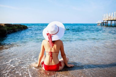 Su yakınında deniz kıyısında oturan bikini kadın arka görünümü.