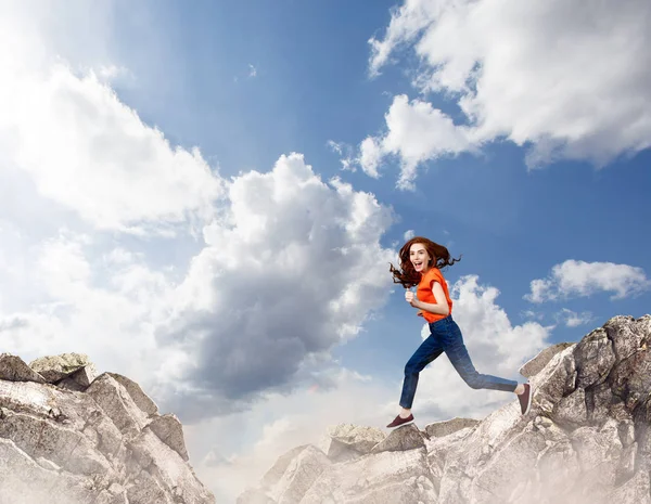 Ruiva mulher salta sobre penhasco no fundo do céu azul . — Fotografia de Stock