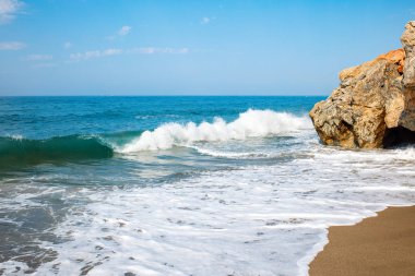 Kumlu plaj ve beyaz köpük ile yumuşak mavi okyanus dalgası.