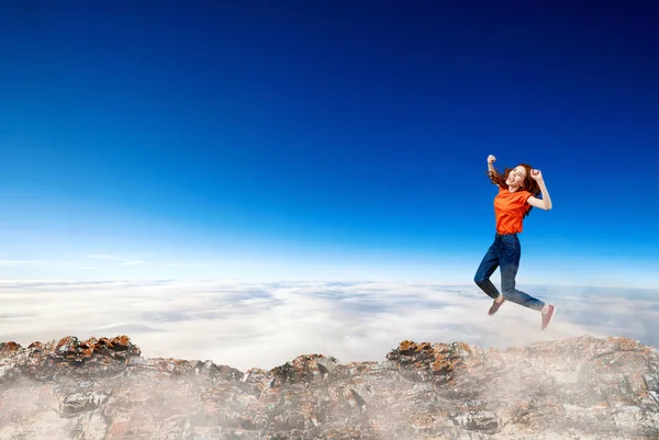 Redhead woman jumps over cliff on blue sky background. — Stock Photo, Image