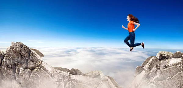 Redhead Woman springt over Cliff op blauwe hemel achtergrond. — Stockfoto