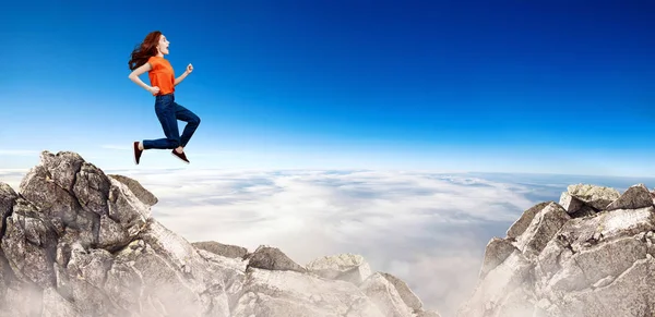 Redhead woman jumps over cliff on blue sky background. — Stock Photo, Image