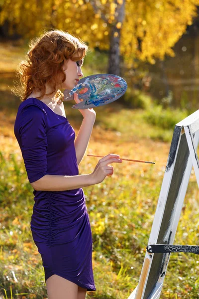 Ung kvinna i sexig klänning målning utomhus i höst parken. — Stockfoto