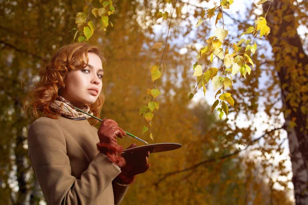 Junge Frau posiert mit Palette und Pinsel im herbstlichen Park. — Stockfoto