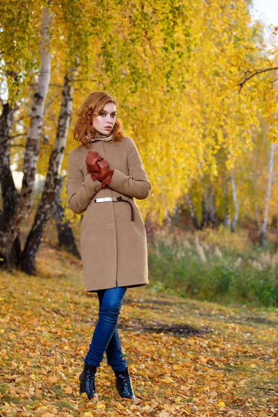 Stylová žena v béžovém kabátě a rukavice stojící na podzimní žluté partě. — Stock fotografie