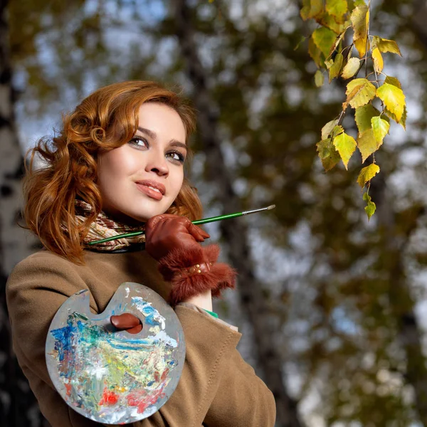 Bella donna con tavolozza e pennello dipinge foglie colori sugli alberi — Foto Stock