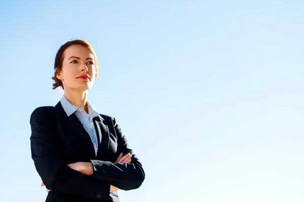 Business woman with crossed hands stands against clear blue sky. — Stock Photo, Image