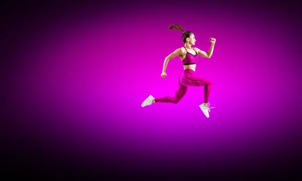 Young woman runner in purple sportswear jump in the air. — Stock Photo, Image