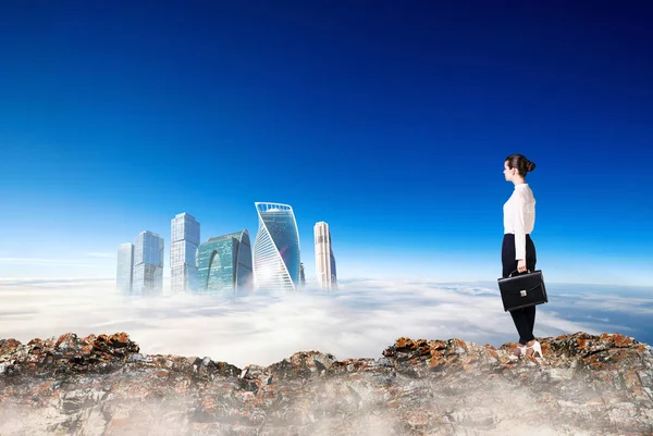 Business woman stands on the edge of mountain and looking on city. — Stock Photo, Image