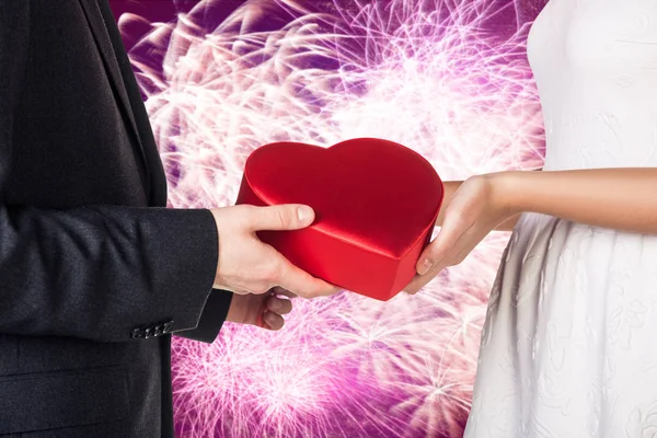 Gros plan mains de jeune couple avec boîte cadeau en forme de coeur rouge . — Photo